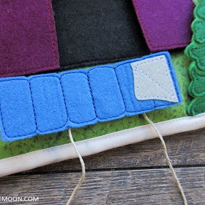 May include: A felt play set with a blue tent, a purple house, a black tent, and a green tree. The tent is attached to the play set with a string.
