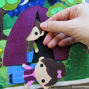 May include: A felt play set with a purple tent, a campfire, and two figures. The figures are a boy and a girl with brown hair. The boy is wearing a brown jacket and blue jeans. The girl is wearing a pink shirt and blue jeans. The tent is open and the boy is peeking out.