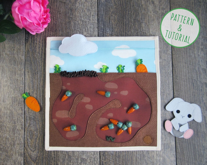 May include: A felt play set featuring a brown rabbit, carrots, and a brown dirt patch with a winding path. The set is designed for children to play with and learn about the world around them.