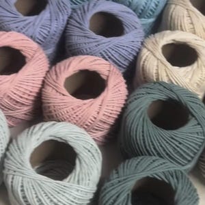 K&ouml;nnte beinhalten: Nahaufnahme von Garnrollen in Pastellfarben wie Rosa, Blau und Creme. Das Garn ist eng um Pappkerne gewickelt. Geeignet f&uuml;r verschiedene Bastelprojekte, mit einer Auswahl an sanften Farbt&ouml;nen.