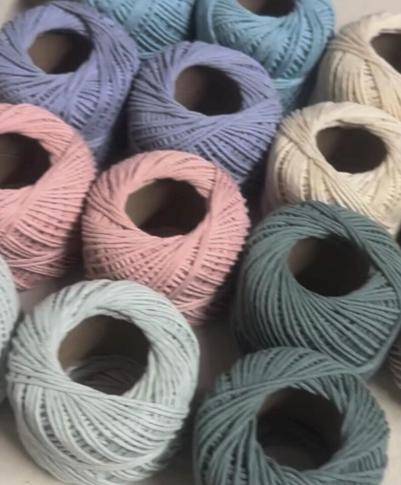 K&ouml;nnte beinhalten: Nahaufnahme von Garnrollen in Pastellfarben wie Rosa, Blau und Creme. Das Garn ist eng um Pappkerne gewickelt. Geeignet f&uuml;r verschiedene Bastelprojekte, mit einer Auswahl an sanften Farbt&ouml;nen.