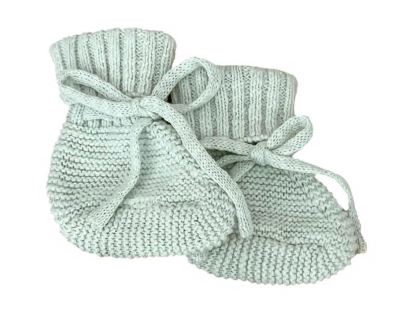 K&ouml;nnte beinhalten: Ein Paar hellgr&uuml;ne gestrickte Babyschuhe. Jeder Schuh hat einen umgeschlagenen Bund und wird mit einem passenden Band gebunden. Die Schuhe sind aus einem weichen, strukturierten Garn gefertigt, ideal f&uuml;r warme kleine F&uuml;&szlig;e.