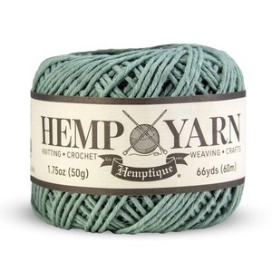K&ouml;nnte beinhalten: Ein Kn&auml;uel aus salbeigr&uuml;nem Hanfgarn mit einem Etikett mit der Aufschrift "HEMP YARN". Das Etikett gibt auch an, dass das Garn zum Stricken, H&auml;keln, Weben und Basteln geeignet ist. Das Kn&auml;uel wiegt 50 g und hat 60 m Garn.