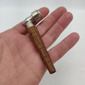 May include: A wooden smoking pipe with a metal bowl and a brown wood finish. The pipe is held in a hand.