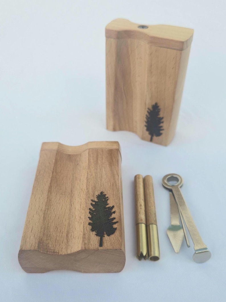 May include: Wooden box set with a carved design and a black tree silhouette. Includes two wooden tubes with brass tips and a metal tool. The set is designed for a specific purpose.