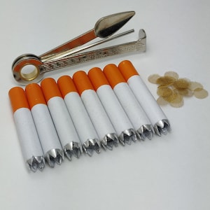 May include: Ten white cigarette tubes with orange tips and silver tips. The tubes are arranged in a row, with the orange tips facing the viewer. A silver cigarette packing tool is in the background.