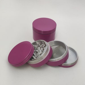 May include: A four-piece pink metal grinder with a screen and a grinding chamber. The grinder is made of metal and has a pink finish.