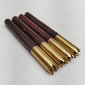 May include: Four wooden and brass arrowheads with a pointed tip. The arrowheads are made of dark wood with a brass tip. The arrowheads are arranged in a row, with the tips pointing to the right.