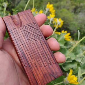 May include: A wooden box with an American flag design carved into the surface. The box has a small opening on the top and is made of a dark reddish-brown wood.