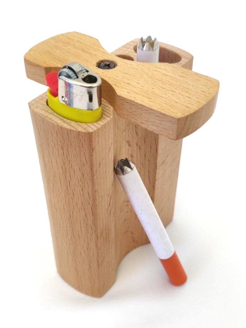 May include: A wooden box with a lighter and a cigarette inside. The box is made of light wood and has a slot for a lighter and a cigarette. The lighter is yellow and has a red top. The cigarette is white with an orange tip.