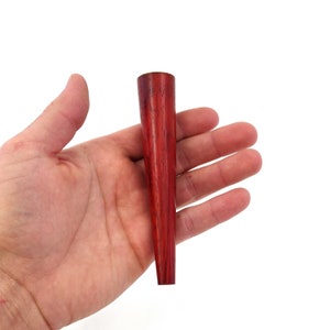 May include: A red wooden pipe with a tapered design. The pipe is held in a hand, showing its size and shape.