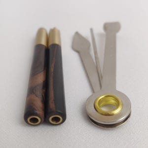 May include: Two wooden smoking pipes with brass tips and a metal pipe tool with a poker, a scraper, and a tamper.