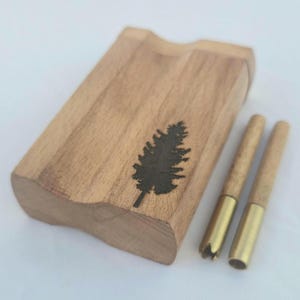 May include: A wooden dugout with a carved tree design and two wooden one-hitters with brass tips. The dugout is rectangular with a curved edge. The tree design is a dark silhouette. The one-hitters have a brass tip and a wooden body.