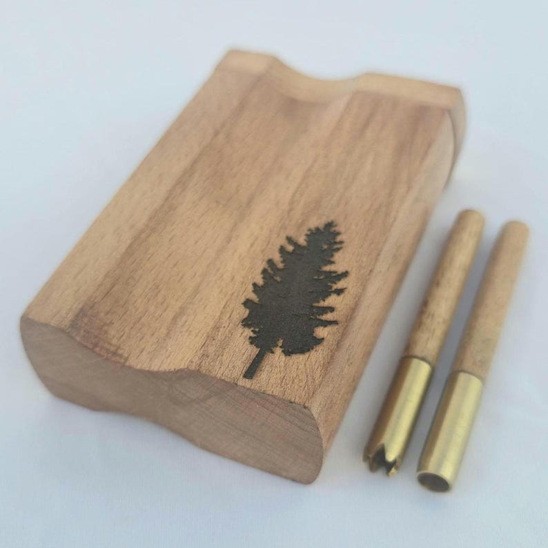 May include: A wooden dugout with a carved tree design and two wooden one-hitters with brass tips. The dugout is rectangular with a curved edge. The tree design is a dark silhouette. The one-hitters have a brass tip and a wooden body.