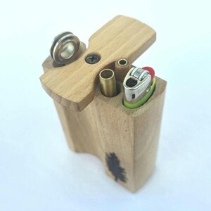 May include: A wooden box with a hinged lid, featuring a lighter, metal tube, and a small metal piece. The box has a tree design on the side. The lighter is silver and green.