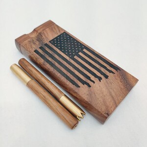 May include: A wooden box and two wooden tools with brass accents. The box features a laser-etched American flag design. The tools are cylindrical with brass tips. The wood has a natural grain and a warm brown color.