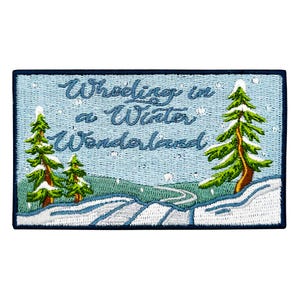 May include: A rectangular embroidered patch featuring a light blue sky with white snowflakes and the text Wheeling in a Winter Wonderland. The scene includes green pine trees with white snow and a snow-covered ground with a path.