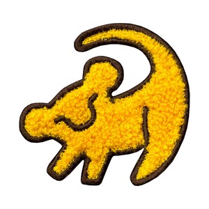 May include: A yellow embroidered patch in the shape of a lion cub, with a brown outline. The patch has a textured, fuzzy appearance. The design is a stylized representation of a lion cub.