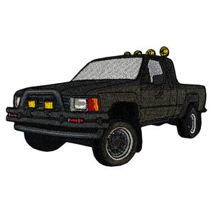 May include: Embroidered patch of a black pickup truck with a roll bar, fog lights, and four yellow lights on the roof. The truck has a silver windshield and black tires. The patch is designed with detailed stitching.