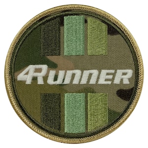 Pode incluir: Um remendo redondo de tecido camuflado verde, marrom e bege com texto bordado branco que diz "4RUNNER". O remendo tem uma borda costurada bege.