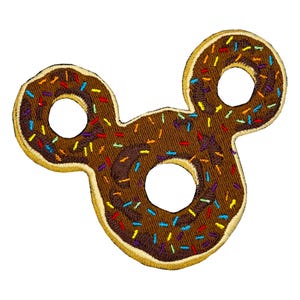 May include: An embroidered patch shaped like three connected donuts, featuring a brown chocolate-colored base with a tan border and colorful sprinkles in red, yellow, blue, and purple scattered across the surface.