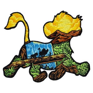 Puede incluir: Parche bordado con forma de cachorro de león, con una cascada, siluetas de animales y una escena de puesta de sol. El parche tiene una cola y una cabeza amarillas, con detalles en marrón, verde y azul. El diseño es detallado y colorido.