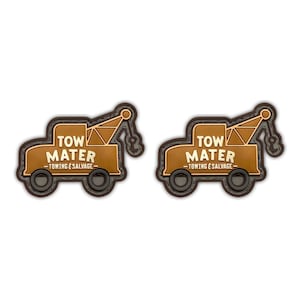 May include: Two brown patches in the shape of a tow truck. The patches have the text "TOW MATER - TOWING & SALVAGE" in white and gold. The tow truck has a brown outline and black wheels.