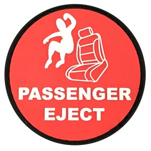 May include: A round, red patch with a black border. The patch features a white graphic of a person being ejected from a car seat, with the words "PASSENGER EJECT" in white block letters.