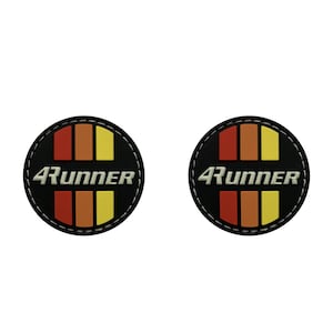 May include: Two black round patches with white stitching around the edges. Each patch has a red, orange, and yellow striped design with the text "4Runner" in white letters.