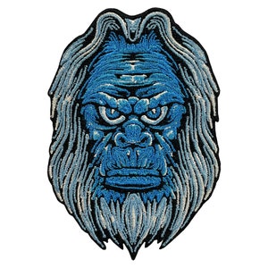 Peut inclure: Patch brodé bleu représentant le visage d'un yéti avec une barbe blanche et un front plissé.
