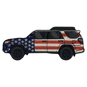 Puede incluir: Parche bordado de un SUV negro con un diseño de bandera estadounidense. La carrocería del vehículo presenta las estrellas y las rayas de la bandera estadounidense. Las ruedas son negras y el parche está sobre un fondo blanco.