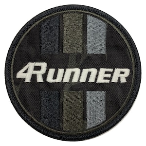 May include: A black, green and grey embroidered patch with the word "4Runner" in white lettering.