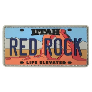 May include: A red, white and blue patch with the text "UTAH RED ROCK LIFE ELEVATED" on it. The patch is shaped like a licence plate.