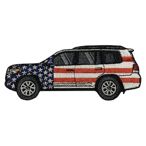 May include: A white SUV with an American flag design. The vehicle is a side profile view with the driver's side facing the viewer. The flag design is on the side of the vehicle and includes red and white stripes and blue stars.