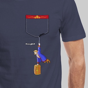 May include: Navy blue t-shirt with a pocket design featuring a cartoon figure hanging from a string. The pocket has a red border with skull accents. The text "*sigh*" is next to the figure. A wooden barrel is below the figure.
