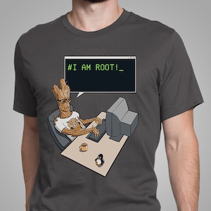 May include: A dark gray t-shirt with a graphic of a cartoon tree-like character sitting at a computer with a penguin beside it. The computer screen shows the text '# I AM ROOT!_'.