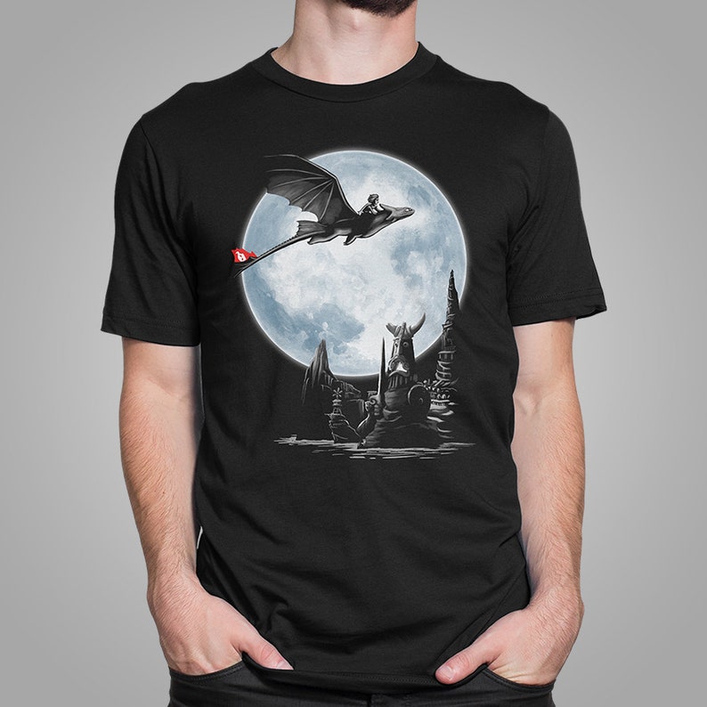 K&ouml;nnte beinhalten: Schwarzes T-Shirt mit einer Fantasy-Grafik eines Drachen und Reiters vor einem Vollmond. Das Design beinhaltet eine wikingerartige Figur und eine rote Flagge mit einem Symbol. Das Kunstwerk ist detailliert.