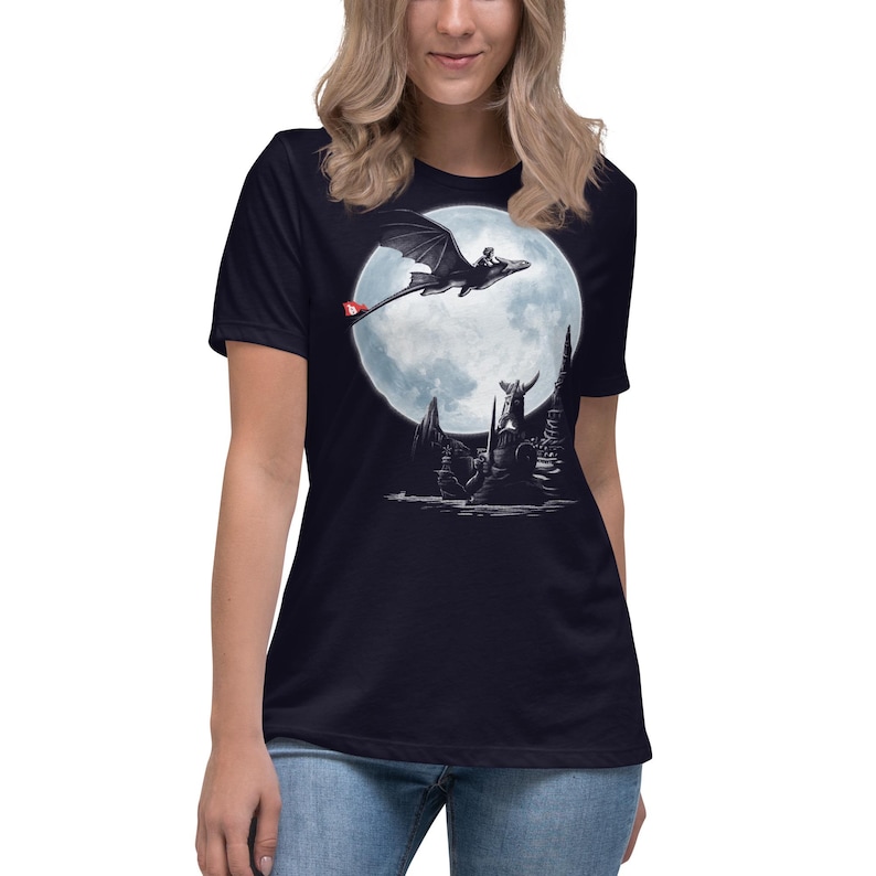 K&ouml;nnte beinhalten: Marineblaues T-Shirt mit einer schwarz-wei&szlig;en Grafik eines Drachen und Reiters vor einem Vollmond. Der Drache hat einen roten Akzent am Schwanz. Das Design beinhaltet eine Fantasy-Landschaft.
