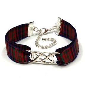 Puede incluir: Un brazalete de cinta de tartán rojo, verde y azul con un dije de nudo infinito plateado y un cierre de cadena plateada.