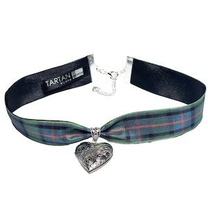 Könnte beinhalten: Eine schwarze Choker-Kette mit einem grün-roten karierten Band und einem silbernen herzförmigen Anhänger. Der Anhänger hat ein filigranes Blumenmuster. Das Band ist vorne an der Kette zu einer Schleife gebunden. Das Etikett auf dem Band lautet "Tartan Works".