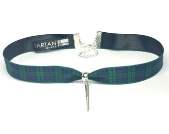May include: A green and blue plaid ribbon choker with a silver charm in the shape of a dagger. The ribbon is tied in a bow at the back of the neck. The charm is attached to a silver chain. The choker is made by Tartan Works.