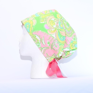 May include: A green, pink, and yellow patterned surgical scrub hat with a pink ribbon tie.