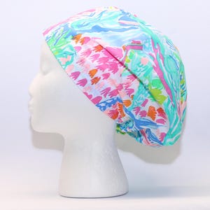 May include: A white scrub hat with a colorful abstract floral print in shades of pink, blue, green, and orange.