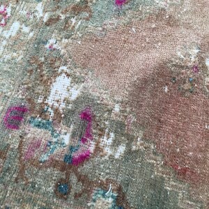 May include: A close-up of a vintage rug with a faded floral pattern in shades of pink, brown, and green.
