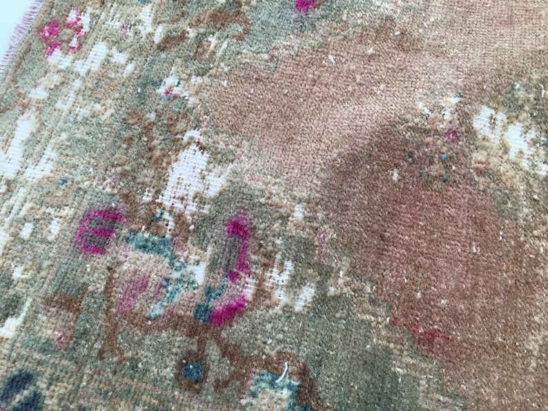 May include: A close-up of a vintage rug with a faded floral pattern in shades of pink, brown, and green.