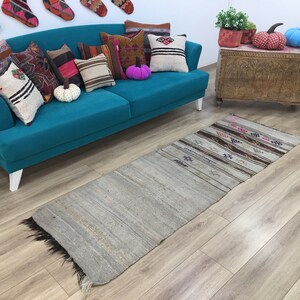 May include: A teal blue sofa with white legs, decorated with colorful throw pillows and a patterned rug. The sofa is in a room with a wooden chest and a yellow chair.