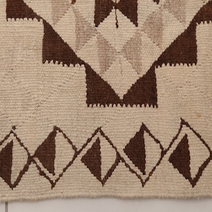 May include: Close-up of a white and brown woven rug with a geometric pattern. The rug has a fringe border.