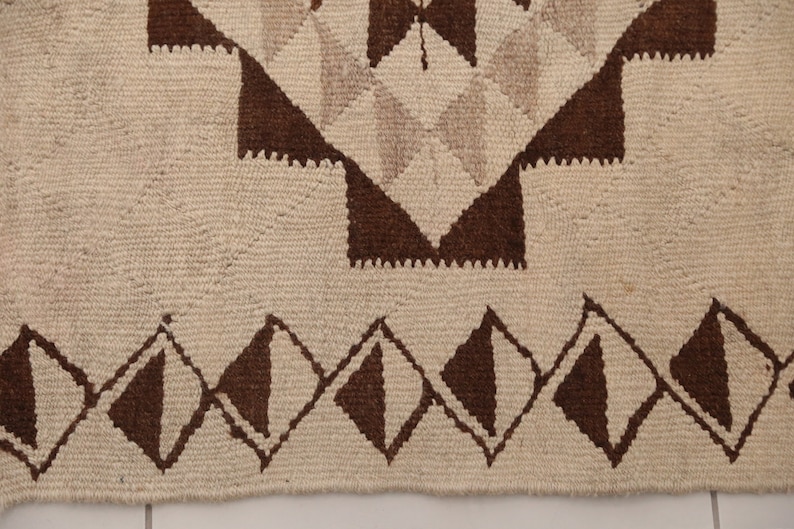 May include: Close-up of a white and brown woven rug with a geometric pattern. The rug has a fringe border.