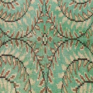 May include: A close-up of a teal green rug with a repeating pattern of brown and white leaves. The rug has a textured surface.