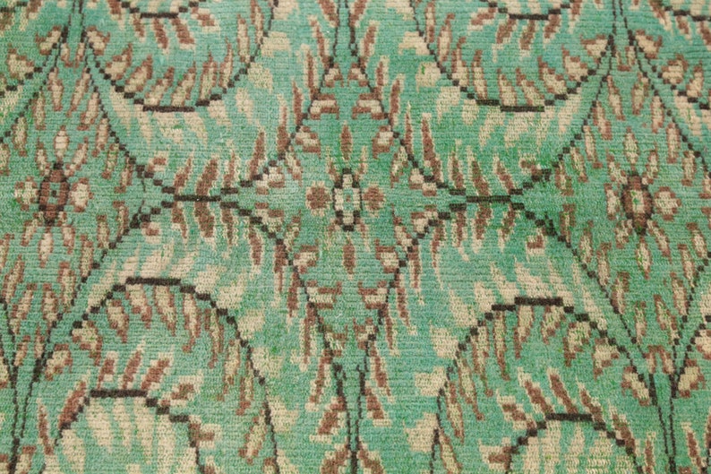 May include: A close-up of a teal green rug with a repeating pattern of brown and white leaves. The rug has a textured surface.